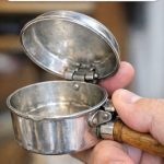 Bought this small silver pan with a hinged lid and a wooden handle at a yard sale. It’s too small for cooking and has a thumb trigger.